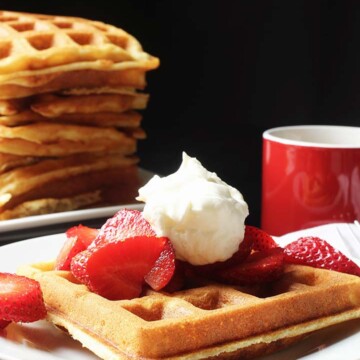 stack of waffles next to a plate with a waffle berries and cream