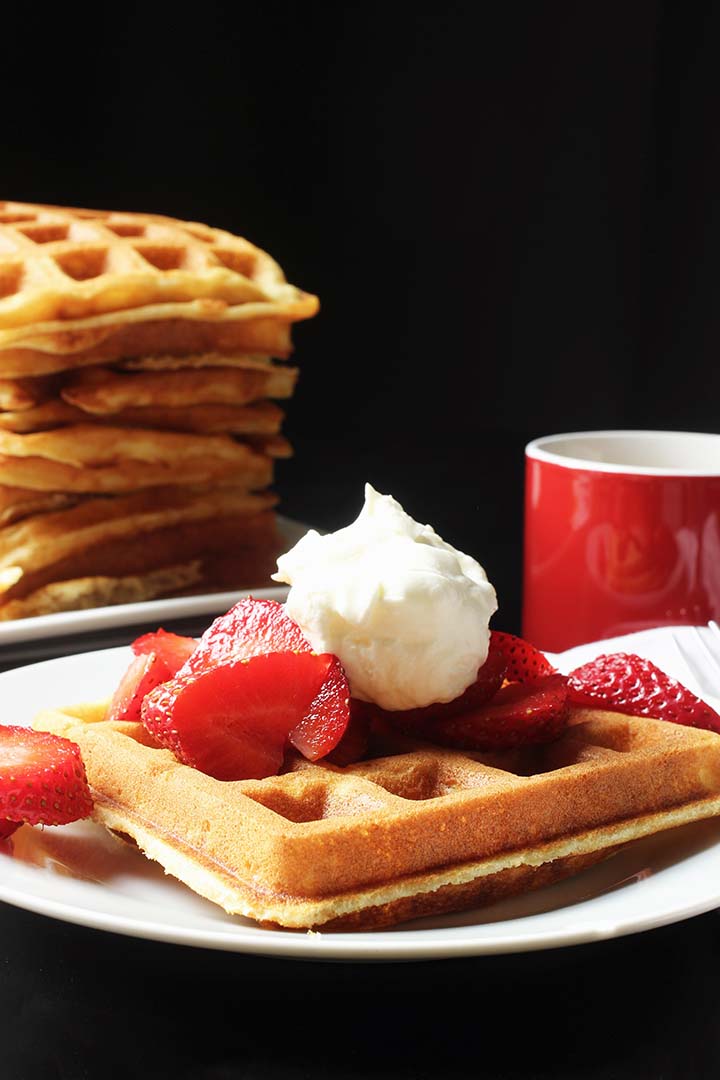 stack of waffles next to a plate with a waffle berries and cream