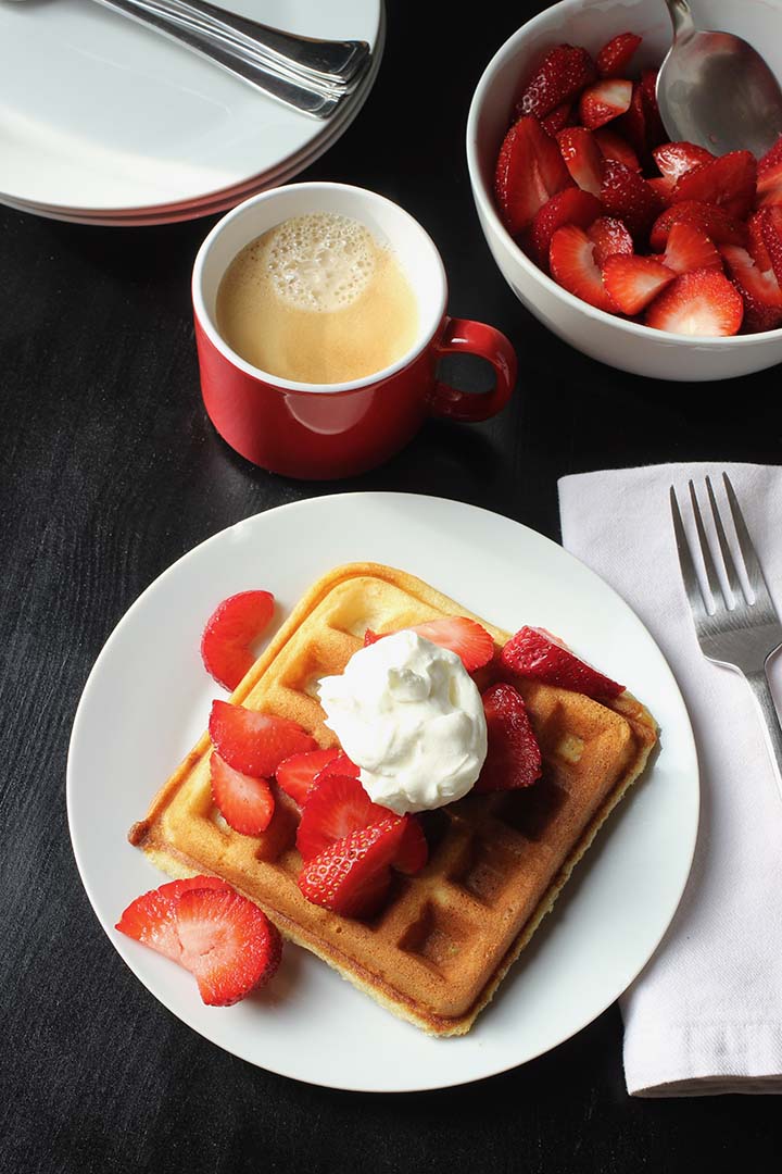 waffle on plate with cup of coffee and berries in bowl