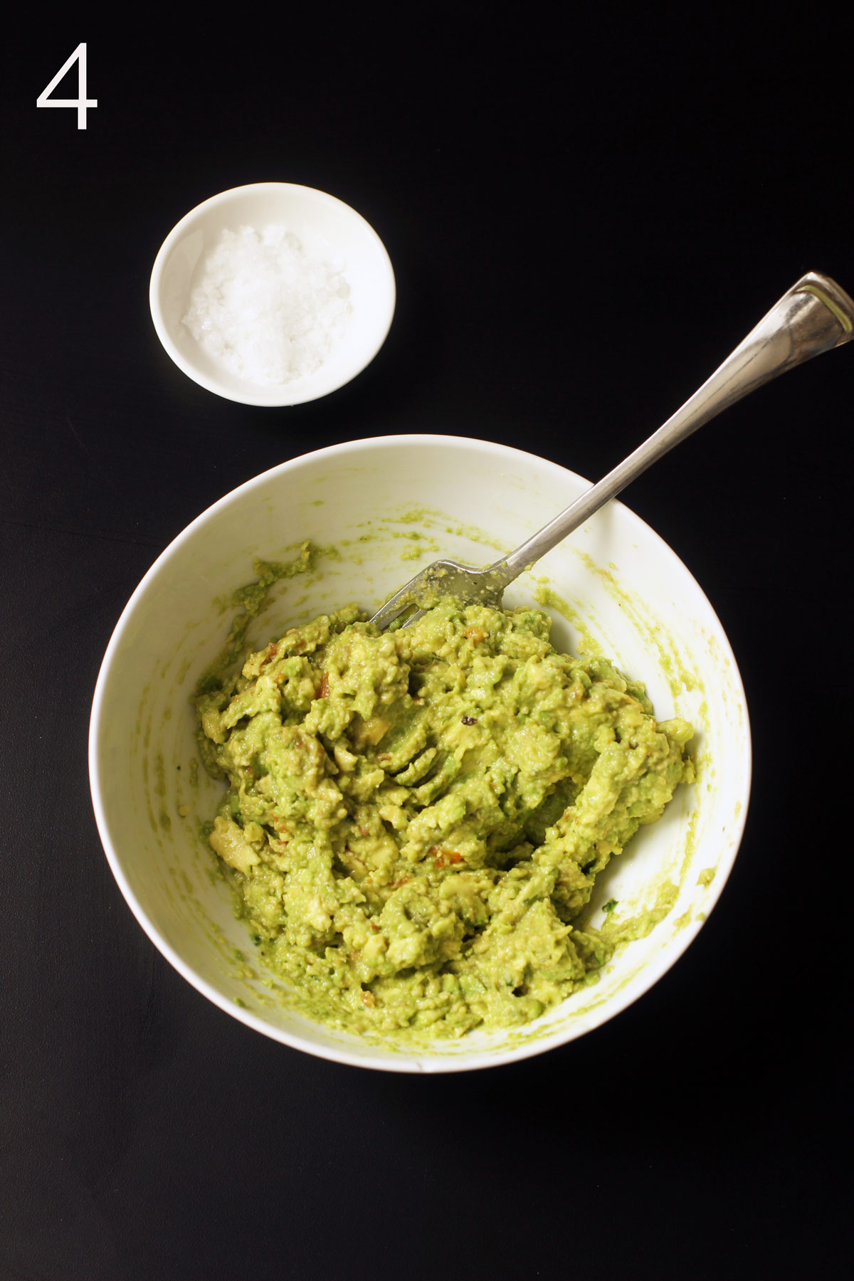 adjusting seasoning and texture of guacamole with fork