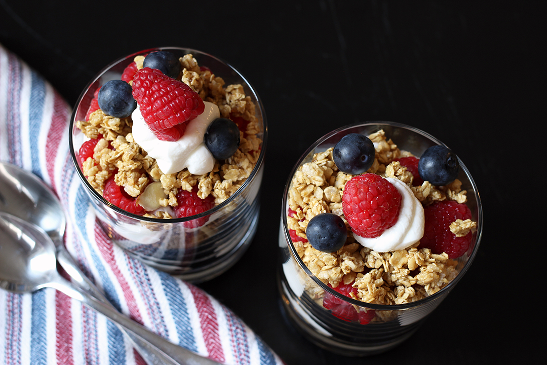 two yogurt parfaits next to napkin and spoons