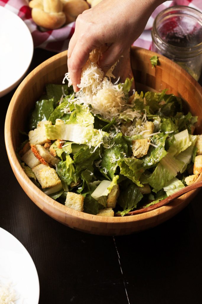 cheese being sprinkled onto a caesar salad