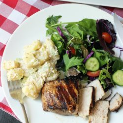 forkful of potato salad on plate with pork chop and salad