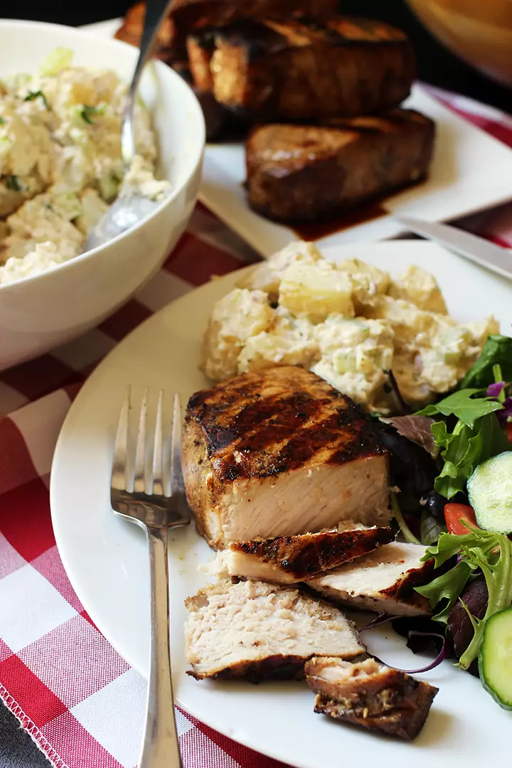 sliced pork chop on plate with fork and side dishes