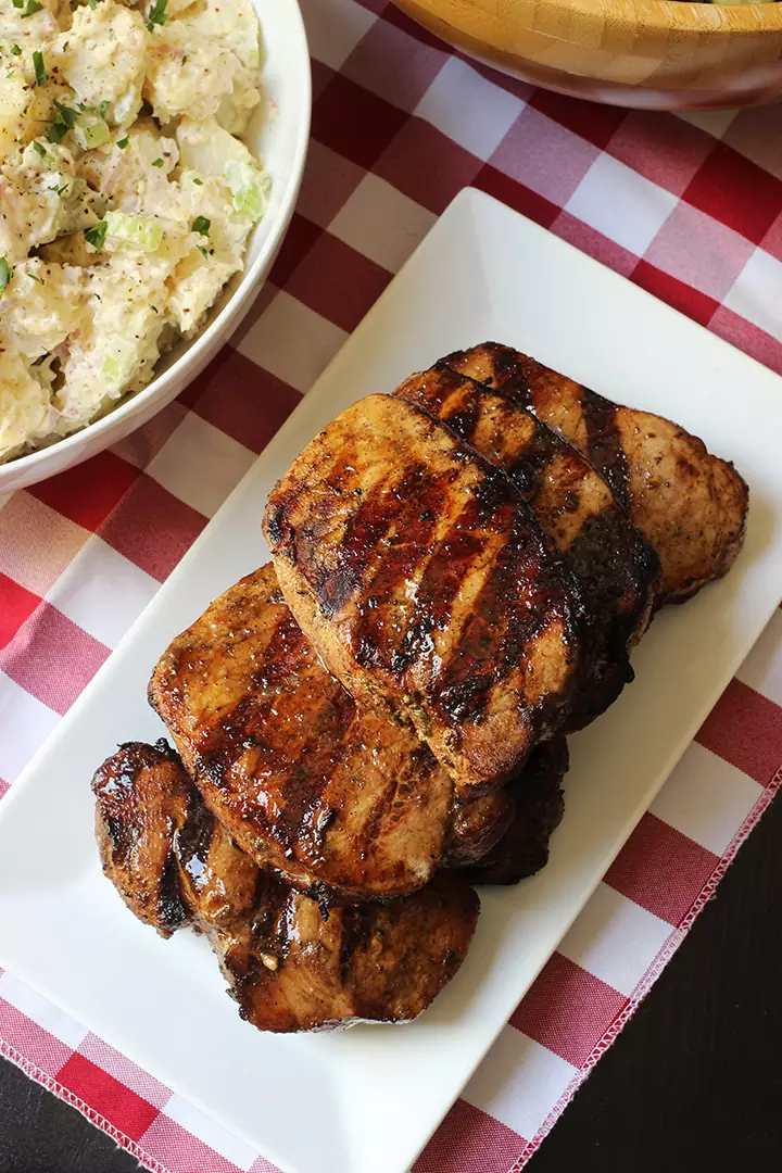 stack of balsamic pork chops on platter on red check cloth