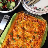 table set with lasagna, salad, and stack of plates