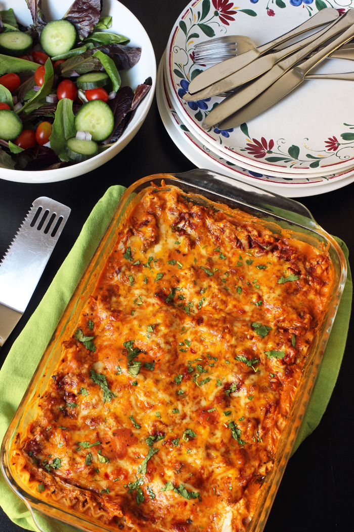 table set with lasagna, salad, and stack of plates