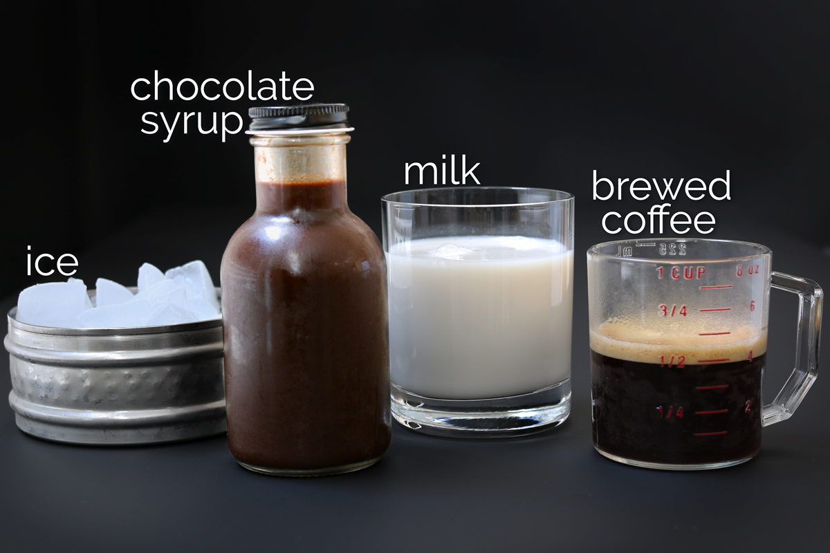 ingredients for iced mocha lined up on black table.