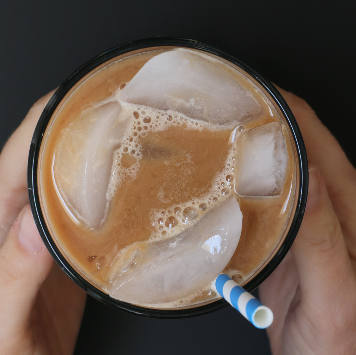 overhead shot of hands clasping glass of iced mocha with ice cubes floating atop.