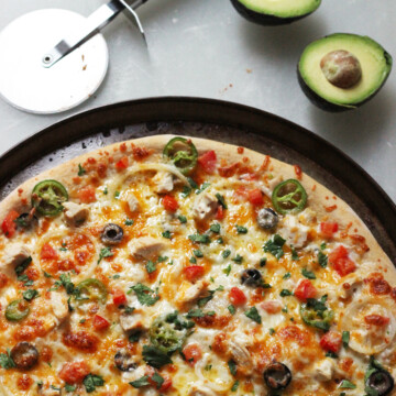 A pizza sitting on top of a pan on a table, with avocado