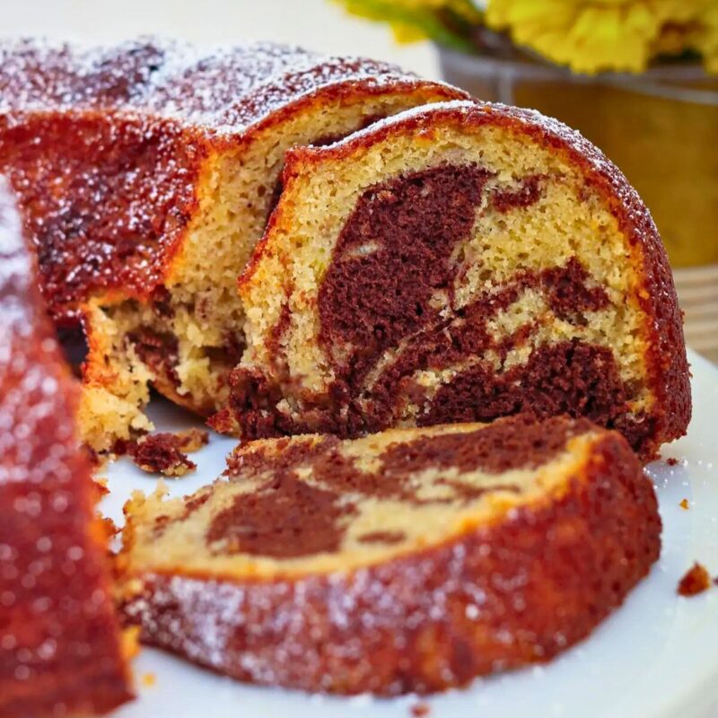 square crop of chocolate banana marble cake on cake stand with yellow flowers in background.
