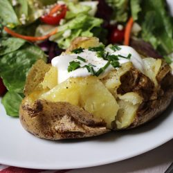 A plate of salad and baked potato with toppings