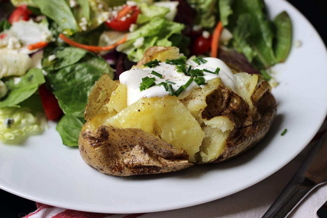 A plate of salad and baked potato with toppings