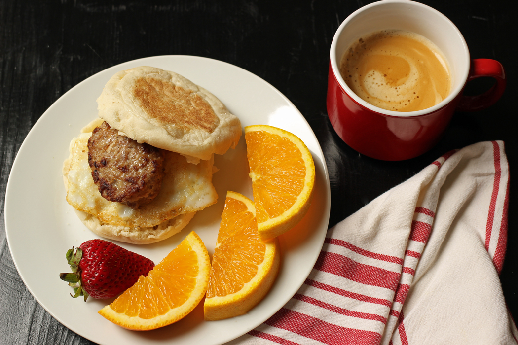 white plate with orange slices and a sausage egg breakfast sandwich