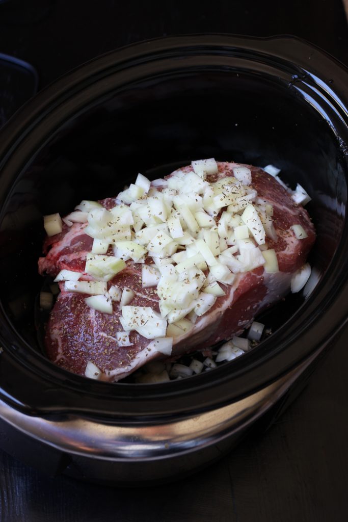 pork roast with seasoning and onions in slow cooker