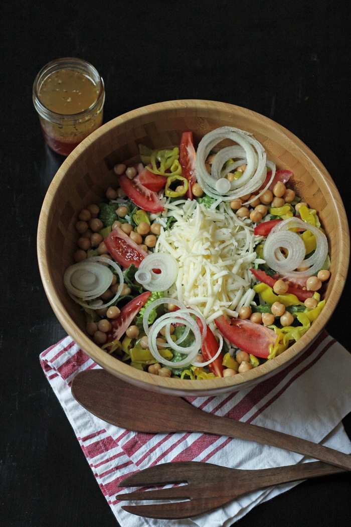 Italian salad in a wooden bowl with fork, spoon, and dressing next to it