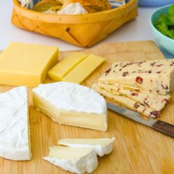 cheese plate with a variety of cheese on wooden board and cheese knife.