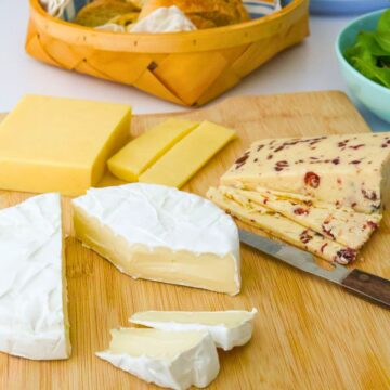 cheese plate with a variety of cheese on wooden board and cheese knife.