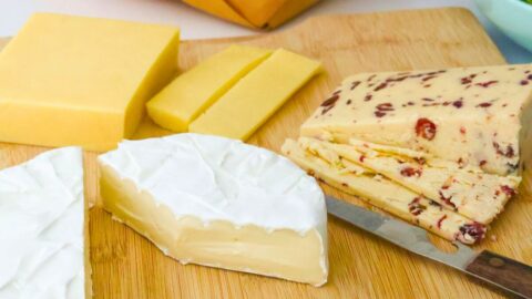 cheese plate with a variety of cheese on wooden board and cheese knife.