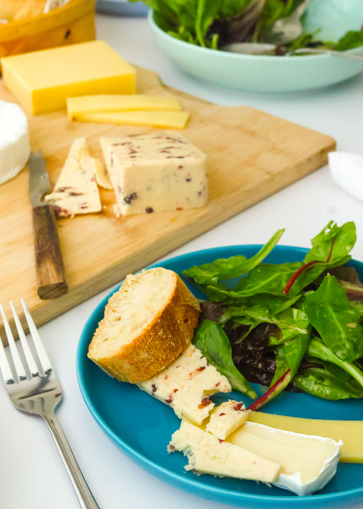 cheese board with plate dished up with a few slices of cheese and some salad and baguette.