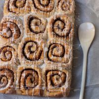 dozen cinnamon rolls on parchment paper with glazing