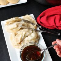 spooning out dipping sauce from platter of potstickers