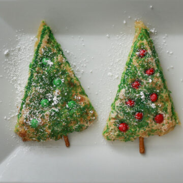 two christmas tree shaped scones on a white platter sprinkled with powdered sugar.