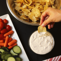 hand dipping potato chip in onion dip
