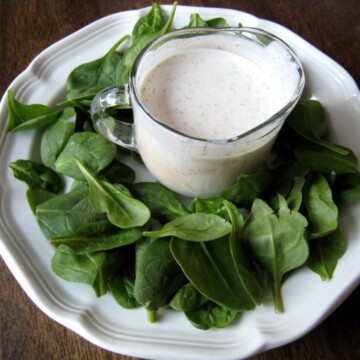pitcher of dressing surrounded by baby spinach