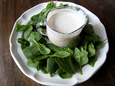 A plate of spinach and dish of Salad dressing