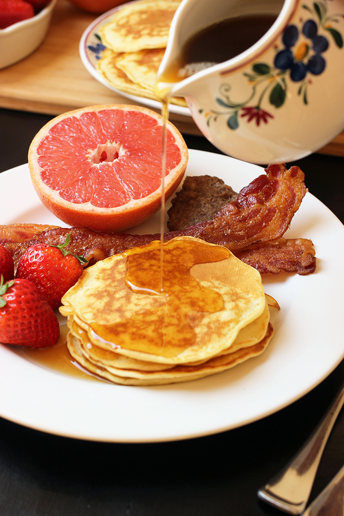 pitcher pouring syrup on stack of pancakes