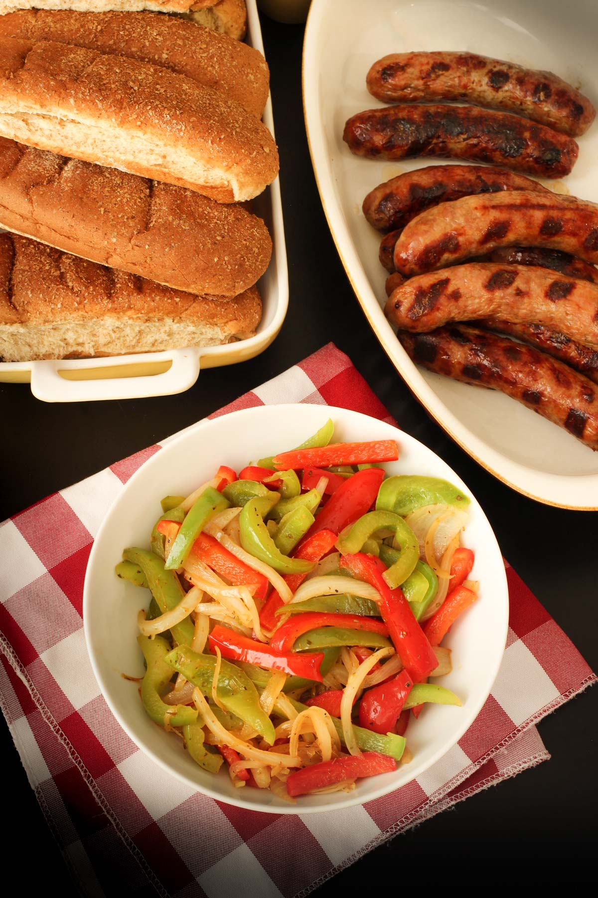 buffet table laid with hot dog buns, brats, and peppers and onions.