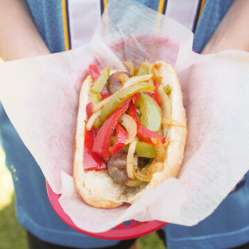 holding bratwurst with peppers and onions