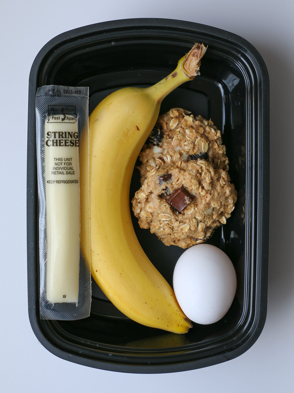 protein cookies in black box with banana, egg, and cheese stick.