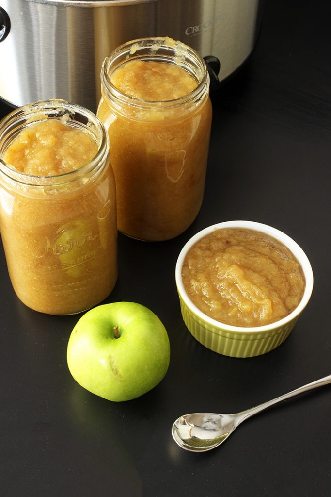 slowcooker applesauce in jars and bowl with apple and spoon on table