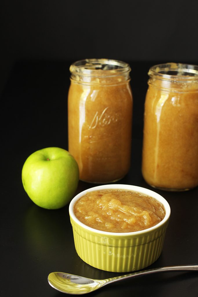 slowcooker applesauce in jars next to bowl of sauce with spoon and green apple