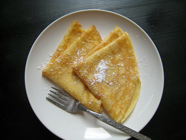 A plate of folded crepes with powdered sugar