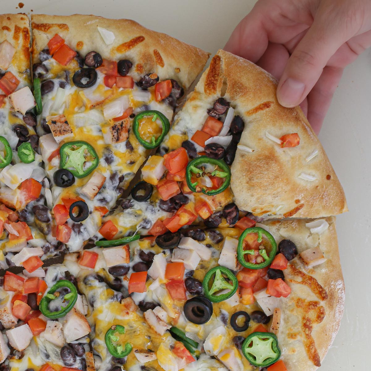 hand pulling a slice of burrito pizza from the whole.