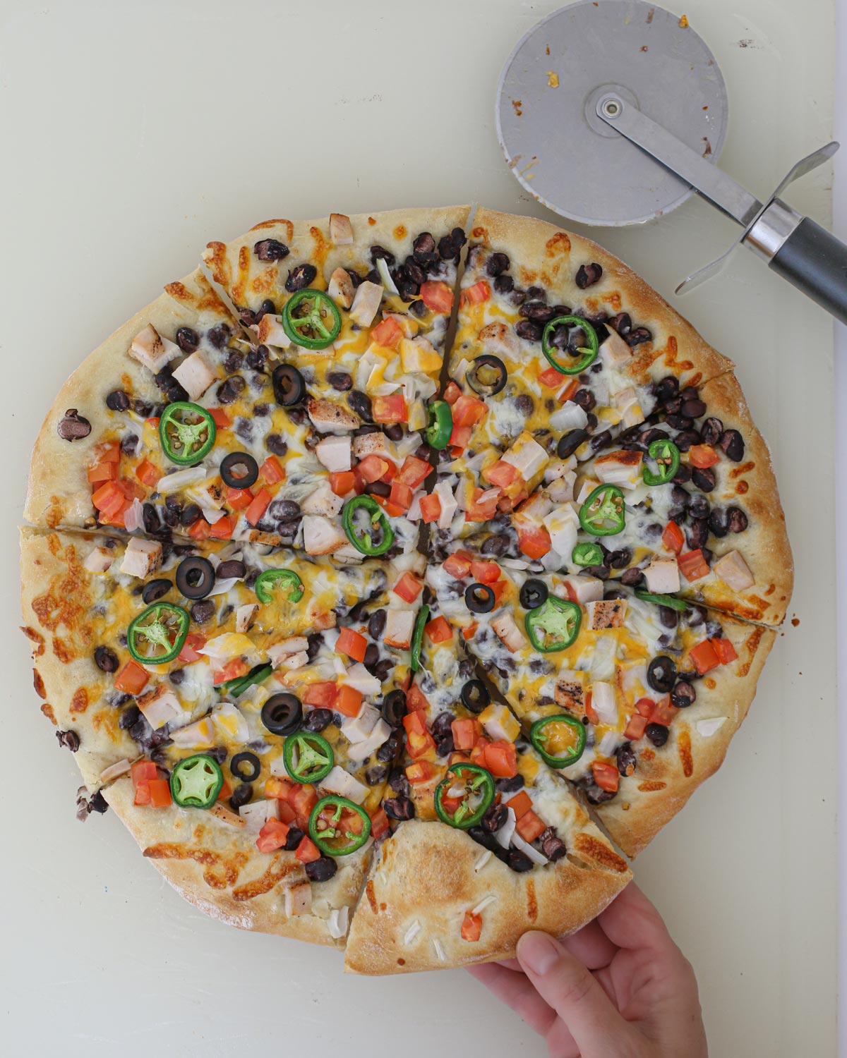 completed black bean pizza, sliced with pizza cutter, woman's hand reaching for a slice.