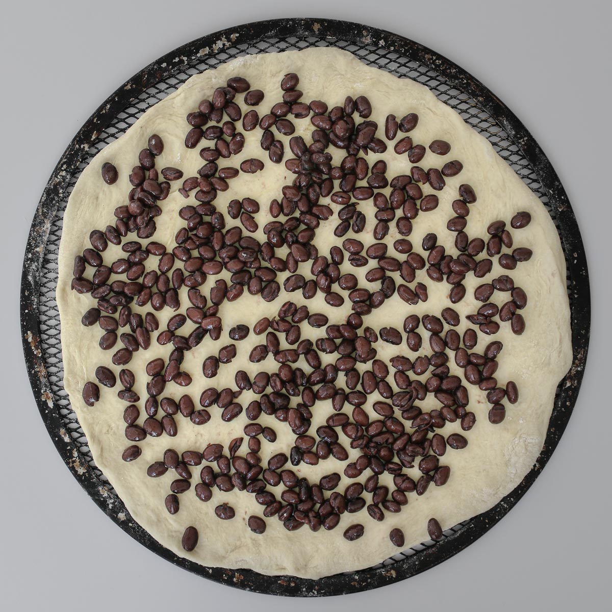 black beans spread on pizza dough on a pizza screen.