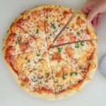 hand reaching for a slice of pizza out of the whole pie.