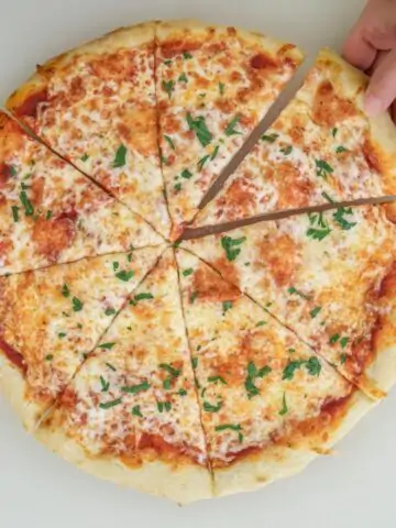 hand reaching for a slice of pizza out of the whole pie.