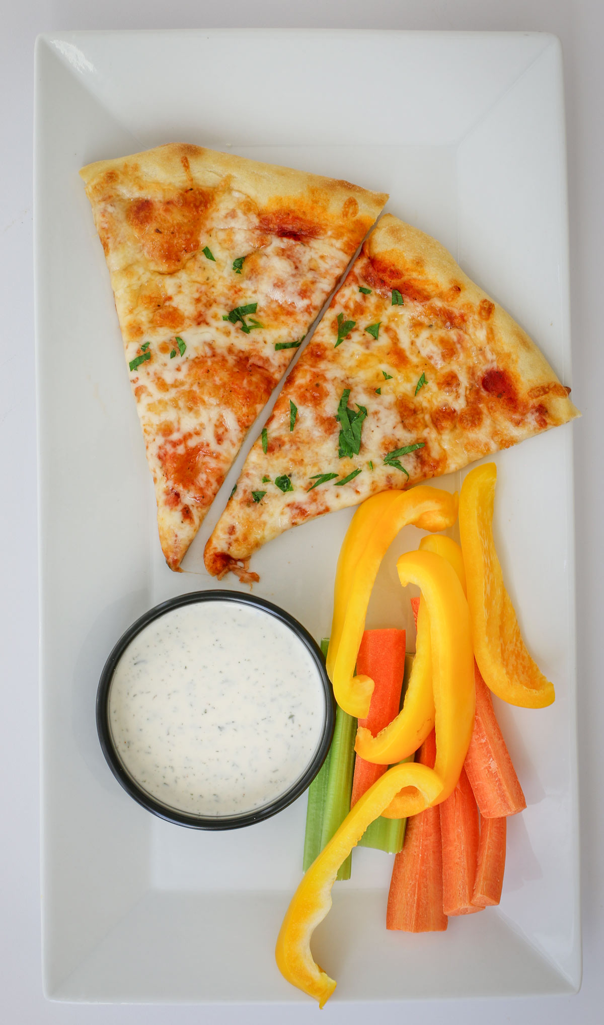 slices of cheese pizza on a plate with veggie dippers and a cup of ranch.