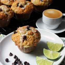 chocolate chip muffin on plate on table next to cooling rack with espresso
