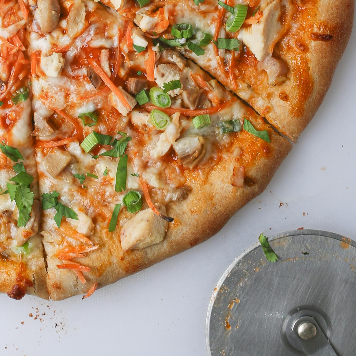 close up of Thai chicken pizza with pizza wheel.