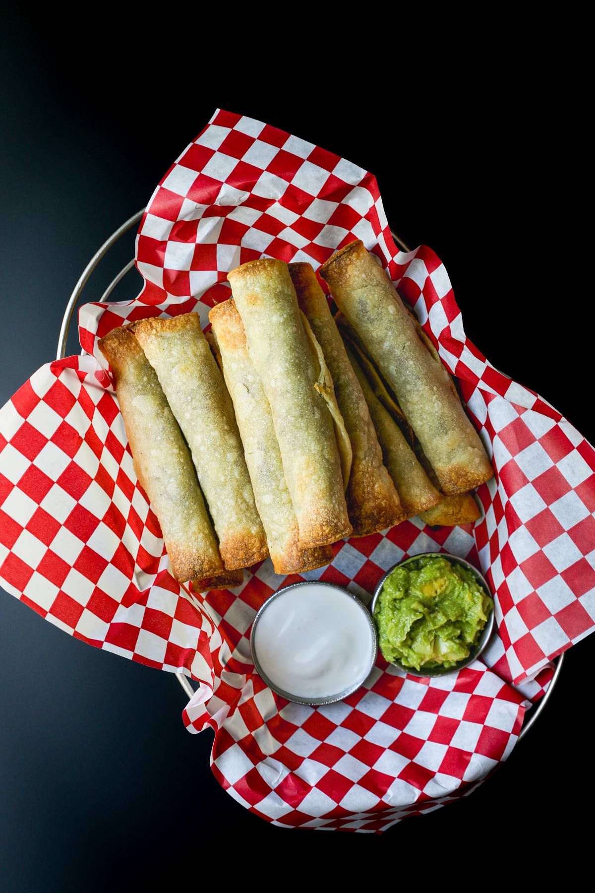 basket of beef taquitos with cups of sour cream and guacamole.