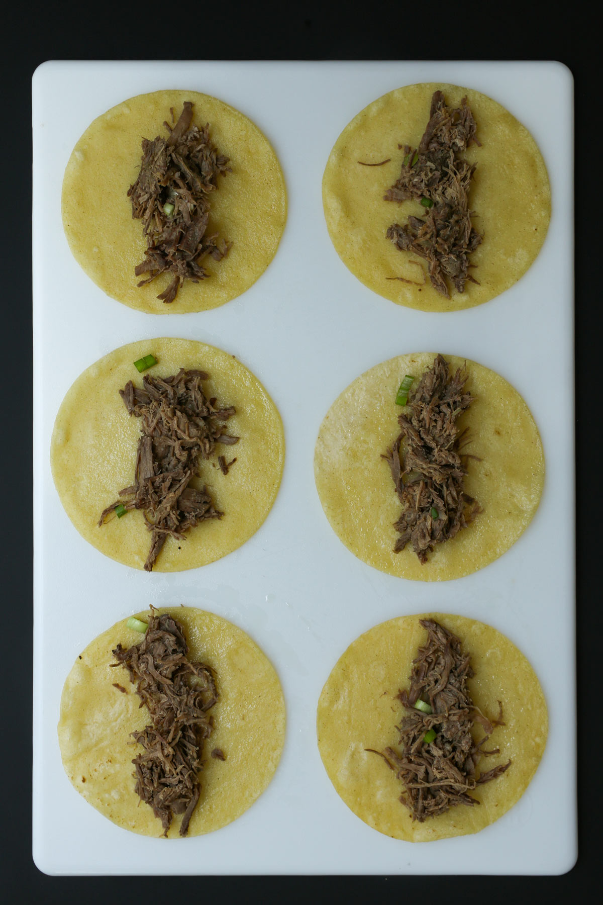 beef filling laid down the center of six tortillas on a white board.