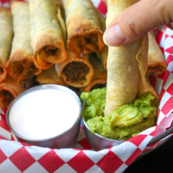 dipping beef taquito into cup of guacamole.