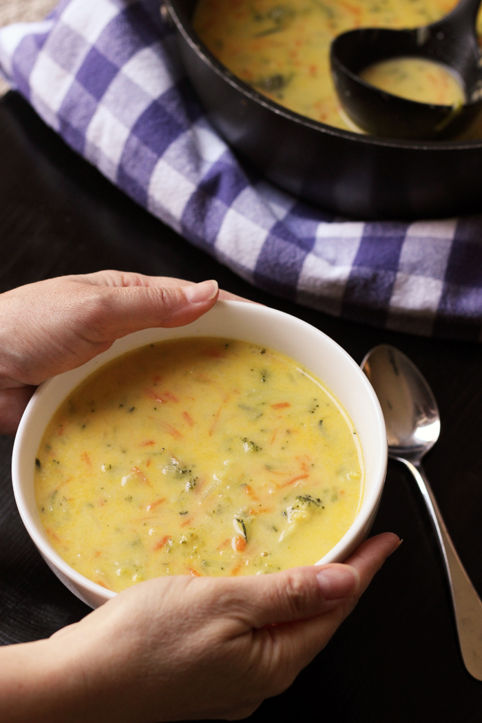 hands holding bowl of cheesy soup