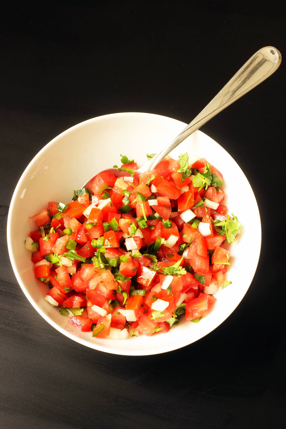 finished bowl of pico de gallo in white bowl with large spoon.